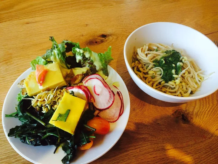 A plate of vegetables and a bowl of noodles on a wooden table