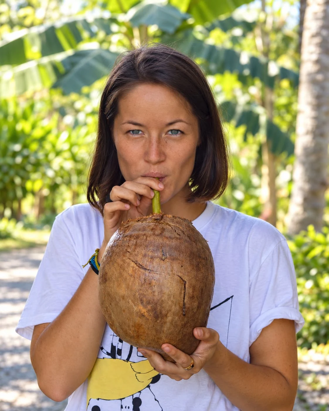 A woman drinking fresh coconut water through a straw in a tropical garden